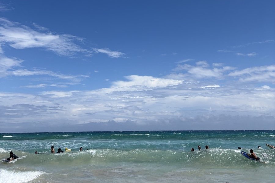 青空の下、白波の立つ海に入って波待ちをしている数人の海水浴客